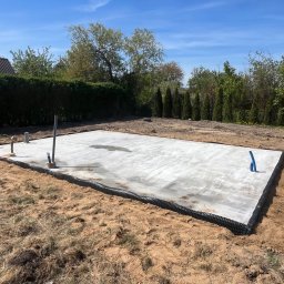 Patryk Kraszewski - Zalany fundament pod budowę domu jednorodzinnego z widocznymi pionowymi rurami instalacyjnymi i zabezpieczeniem przeciwwilgociowym na obrzeżach.