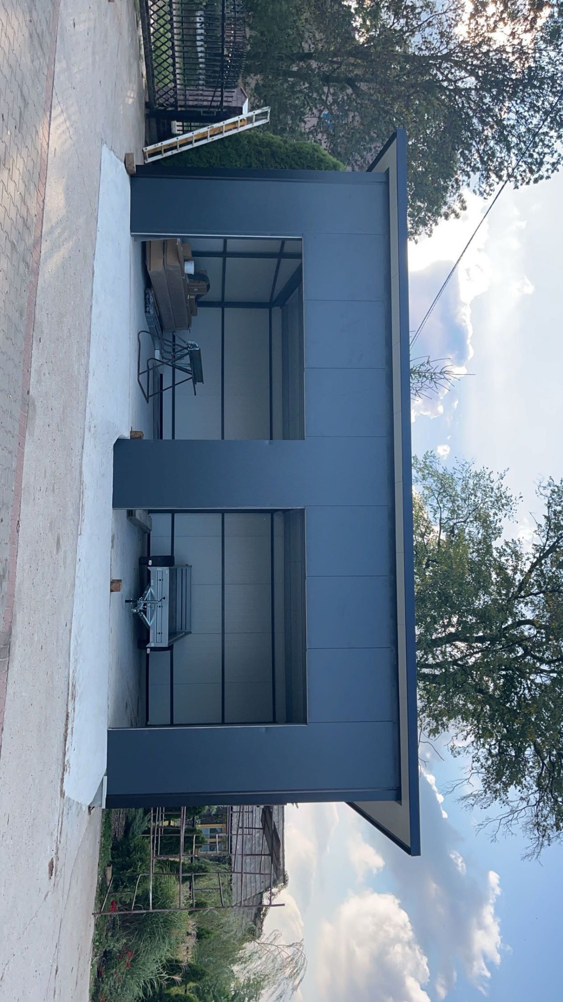 Nowoczesny, dwustanowiskowy garaż blaszany w kolorze grafitowym, z widocznym wyposażeniem wewnątrz, na tle betonowej wylewki i drzew