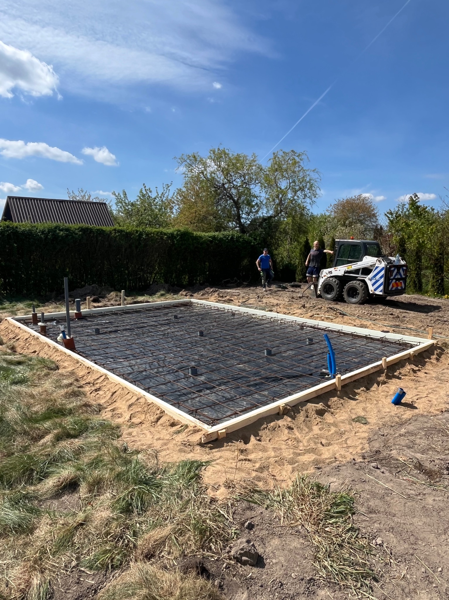 Przygotowany teren pod wylewkę fundamentową z deskowaniem i zbrojeniem siatką. W tle widoczny miniładowarka oraz dwie osoby.