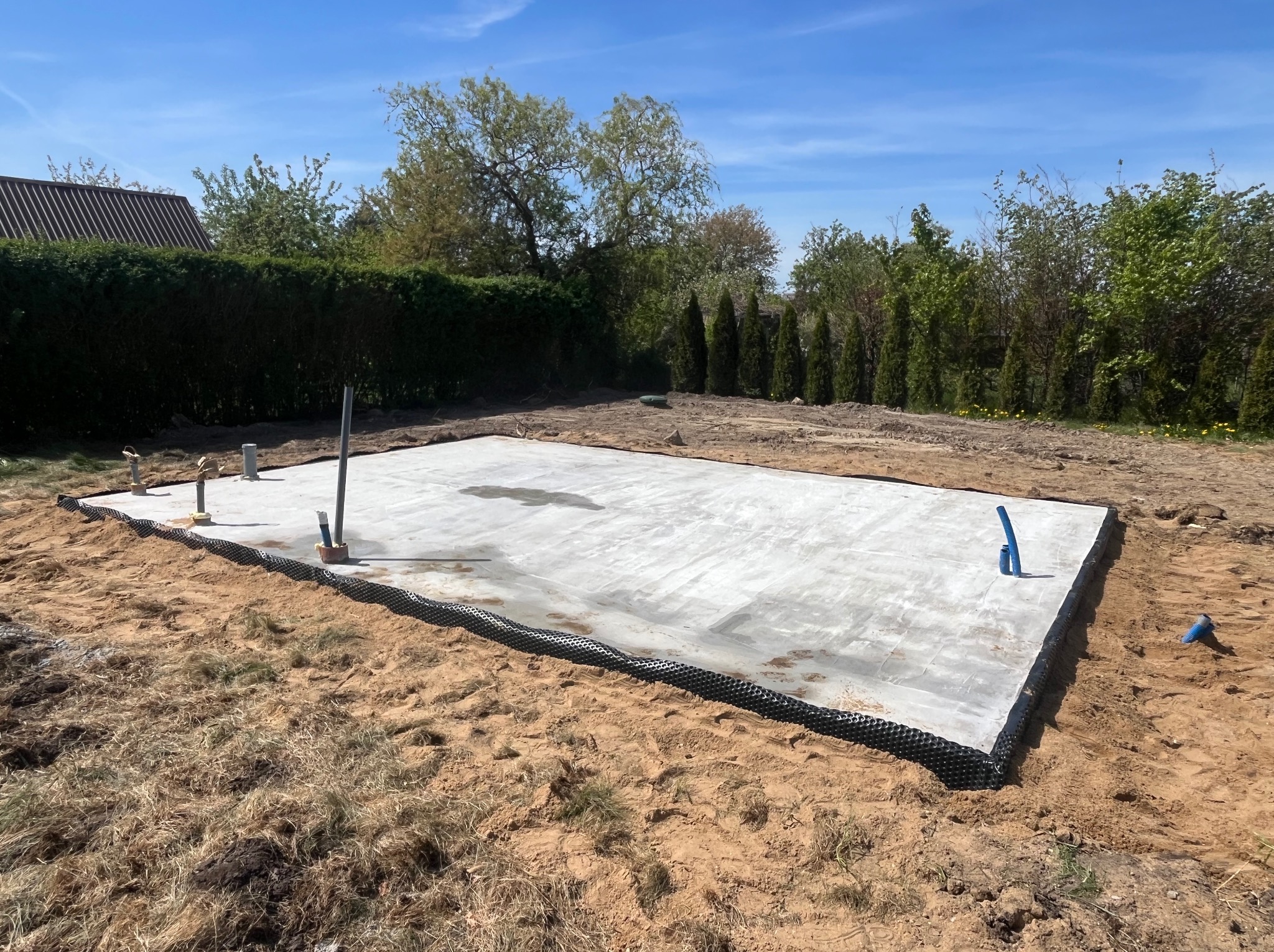 Zalany fundament pod budowę domu jednorodzinnego z widocznymi pionowymi rurami instalacyjnymi i zabezpieczeniem przeciwwilgociowym na obrzeżach.