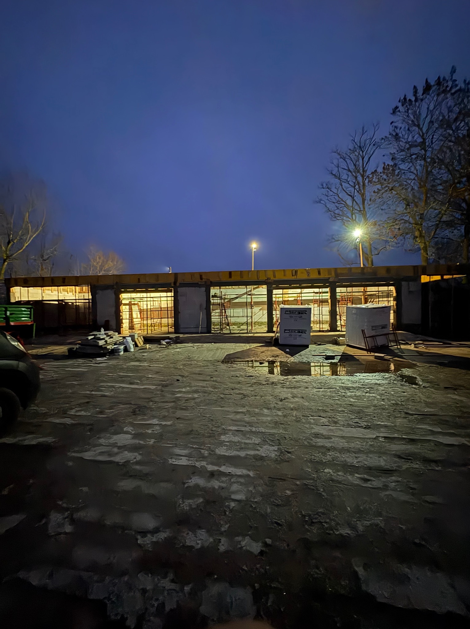 Wczesnym rankiem widok na budowę w stanie surowym otwartym. Widoczne bloczki, zbrojenia i szalunki. Na pierwszym planie teren budowy z kałużami.