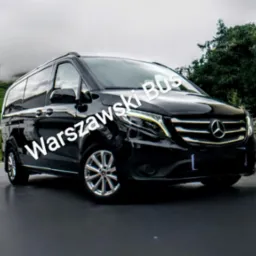 Czarny Mercedes-Benz Vito z napisem 'Warszawski Bus' na tle zielonego wzgórza i drzew w mglisty dzień.