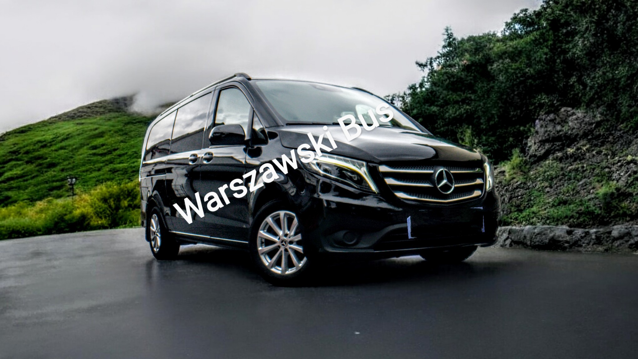 Czarny Mercedes-Benz Vito z napisem 'Warszawski Bus' na tle zielonego wzgórza i drzew w mglisty dzień.