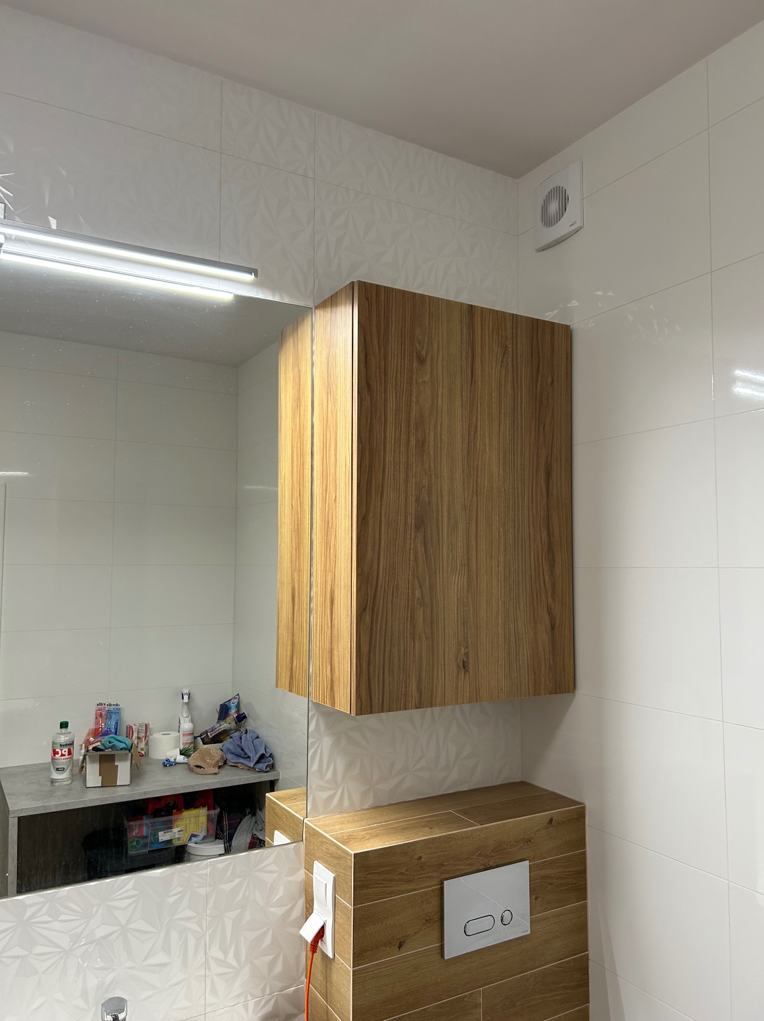 Nowoczesna łazienka z wiszącą szafką z drewnopodobną okleiną, białe płytki z geometrycznym wzorem i lustro z oświetleniem LED.