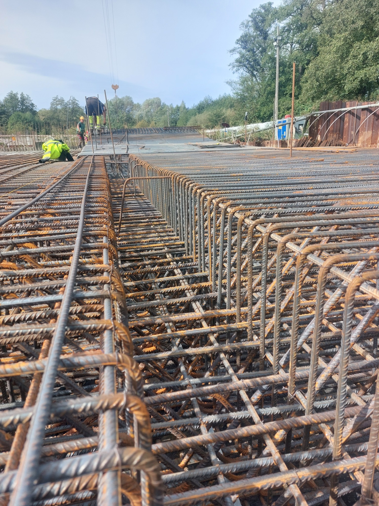 Siatka zbrojeniowa na budowie w Tychach, widoczne elementy konstrukcyjne i pracownicy w oddali, przygotowanie do zalewania betonem.