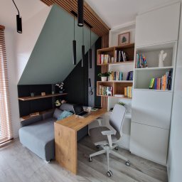 WOOD MEBLE SPÓŁKA Z OGRANICZONĄ ODPOWIEDZIALNOŚCIĄ - Pokój na poddaszu ze strefą pracy: szara sofa z półkami, biurko z drewnianym blatem, białe regały na książki i szare krzesło biurowe na kółkach, oświetlenie punktowe.