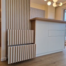 WOOD MEBLE SPÓŁKA Z OGRANICZONĄ ODPOWIEDZIALNOŚCIĄ - Nowoczesna zabudowa kuchenna z białymi frontami i drewnianymi lamelami, otwarte szuflady z lamelami, widoczny fragment blatu i oświetlenie sufitowe