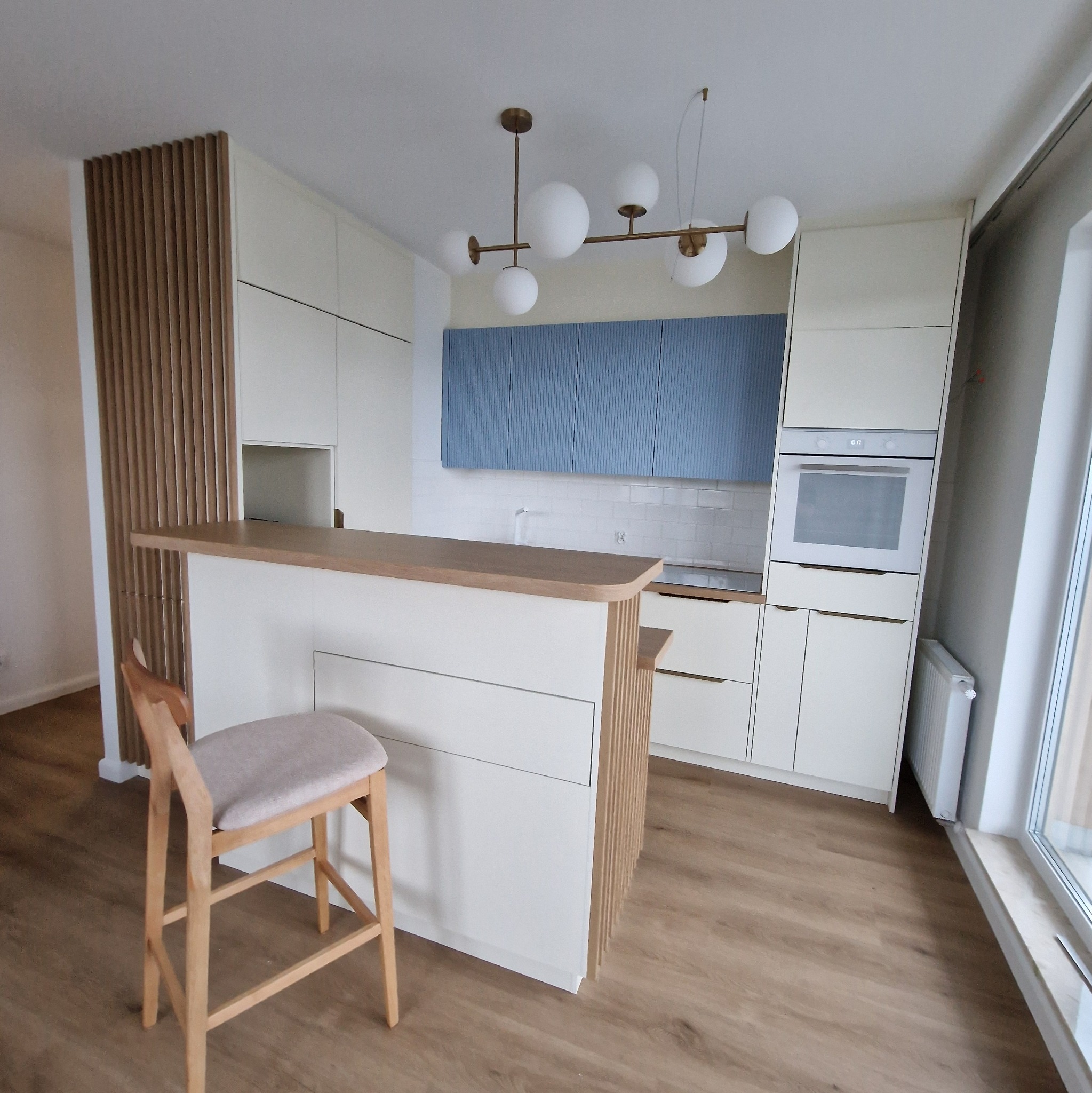 Nowoczesna kuchnia z białymi szafkami, niebieskimi akcentami i drewnianym blatem w Gdańsku, widok na wyspę kuchenną z hokerem.