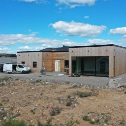 Bona Małgorzata Ptach - Montaż okien aluminiowych w nowoczesnym domu z drewnianą elewacją, widoczne narzędzia pracy i samochód dostawczy firmy.