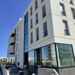 Bona Małgorzata Ptach - Nowoczesny budynek w trakcie wykończenia z dużymi przeszkleniami i balkonami, widoczne materiały budowlane na pierwszym planie.