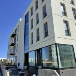 Nowoczesny budynek w trakcie wykończenia z dużymi przeszkleniami i balkonami, widoczne materiały budowlane na pierwszym planie.