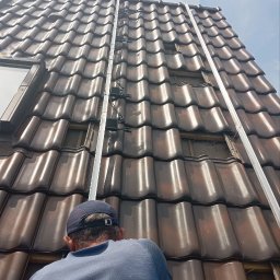 Integral Electrics and Constuction - Montaż konstrukcji wsporczej pod panele słoneczne na dachu z brązowej dachówki ceramicznej, widoczne elementy mocujące i fragment okna dachowego.