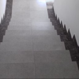 Integral Electrics and Constuction - Wykończone schody wewnętrzne z szarymi płytkami i ciemnym, marmurkowym wykończeniem przy ścianach, widok z góry.