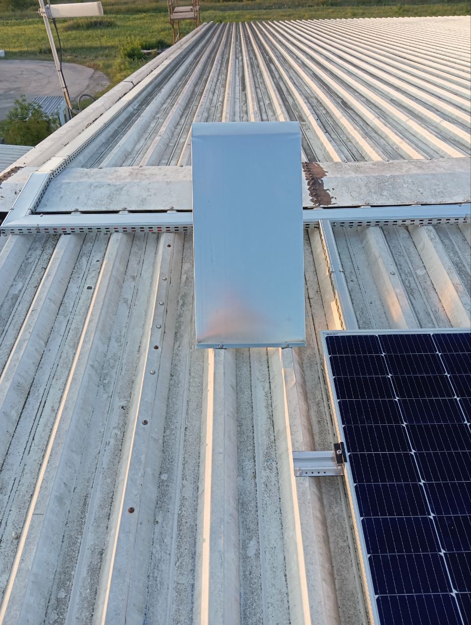 Panel fotowoltaiczny zamontowany na metalowym dachu z widoczną konstrukcją wsporczą i elementem wentylacyjnym.