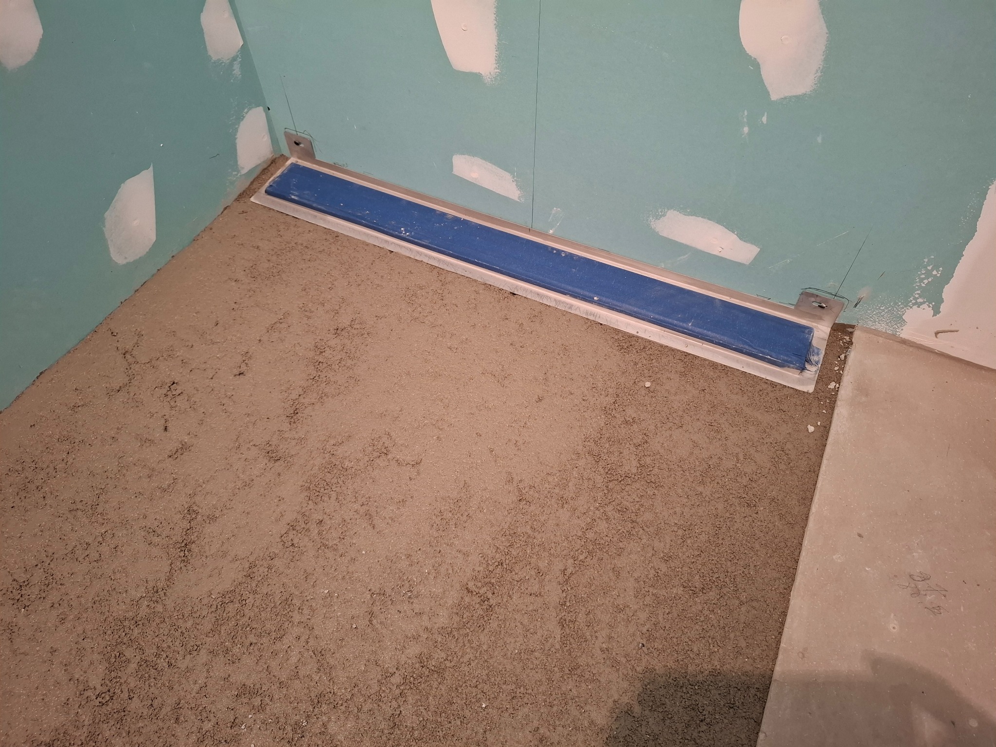 Przygotowanie podłoża pod prysznic z odpływem liniowym w łazience, widoczne płyty gipsowo-kartonowe na ścianach z miejscami po szpachlowaniu.