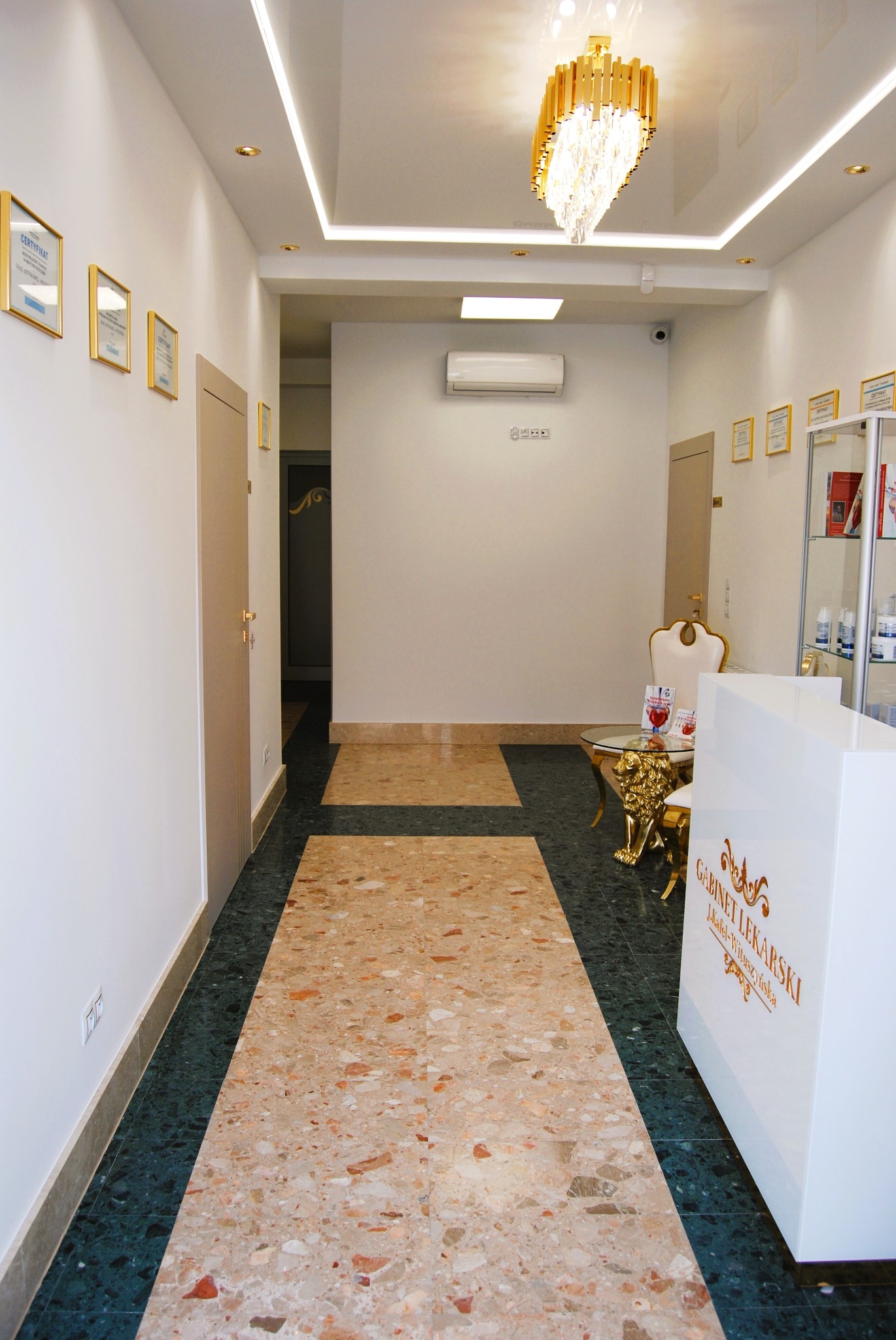 Jasne wnętrze gabinetu lekarskiego z marmurową podłogą, złotym żyrandolem i recepcją z napisem 'Gabinet Lekarski'