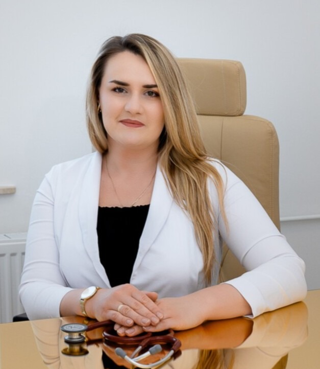 Portret kobiety lekarza w białym fartuchu, ze stetoskopem na biurku, w gabinecie o jasnych ścianach.