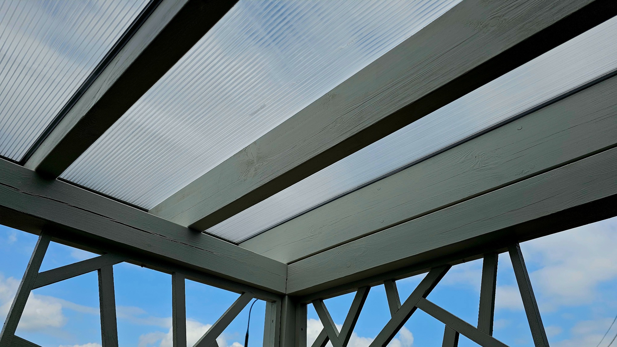 Drewniana konstrukcja z przezroczystym zadaszeniem, widok z dołu na błękitne niebo przez ażurowe boki.