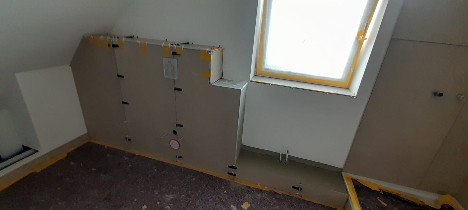 Poddasze w trakcie zabudowy płytami gipsowo-kartonowymi, widoczne profile, taśmy maskujące, otwór okienny dachowy.