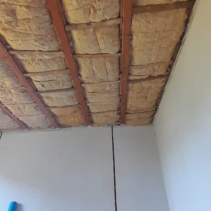 Izolacja stropu wełną mineralną pomiędzy drewnianymi belkami, widoczne fragmenty ściany z płyt kartonowo-gipsowych.