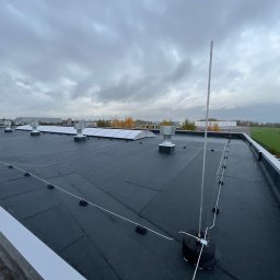 Diego Service - Widok z góry na płaski dach budynku przemysłowego z zainstalowaną instalacją odgromową, widoczne przewody i maszt odgromowy na tle pochmurnego nieba.