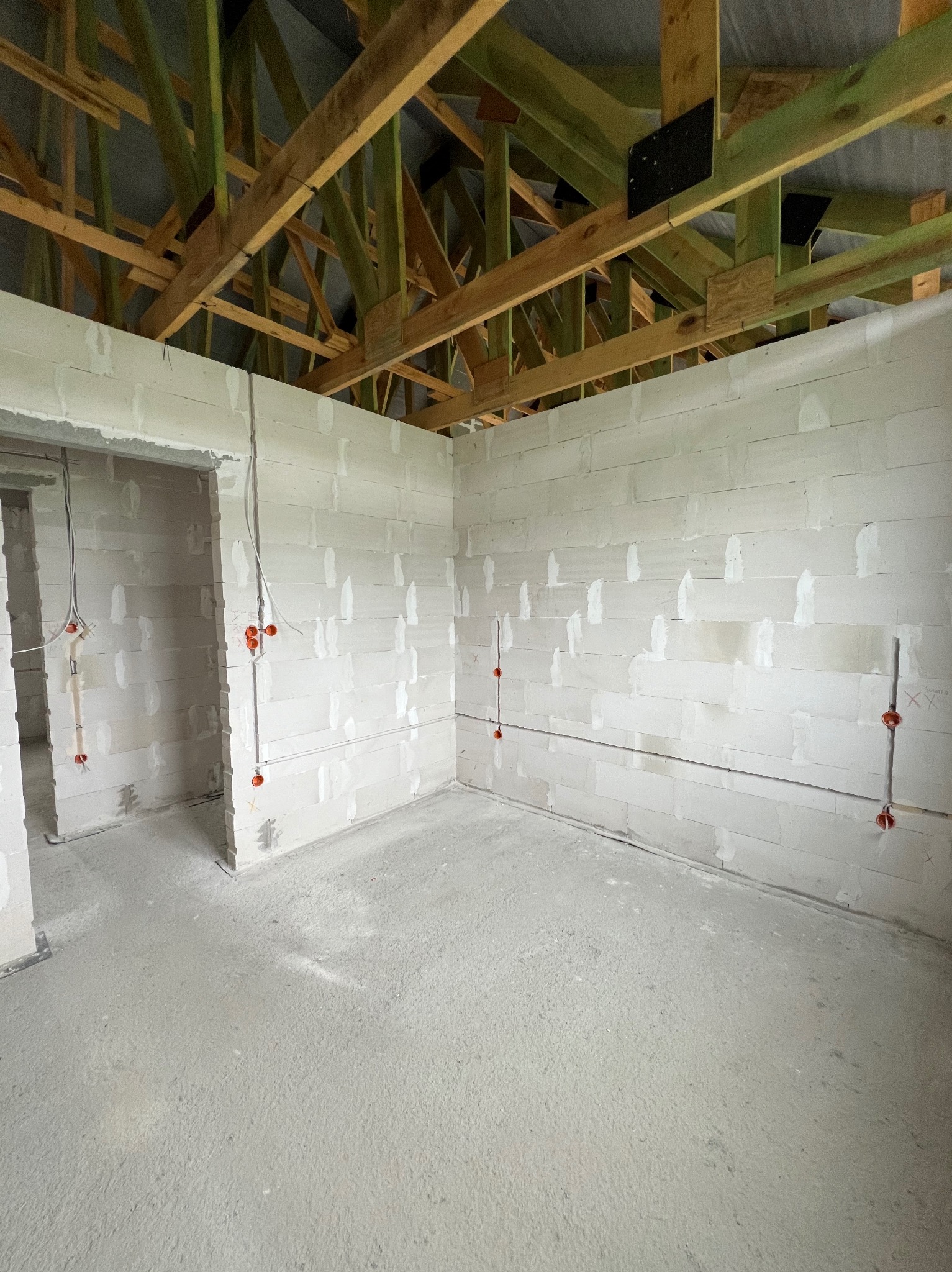 Surowy stan wnętrza w trakcie budowy, widoczne ściany z betonu komórkowego z poprowadzonymi przewodami elektrycznymi w peszlach, drewniana konstrukcja dachu.