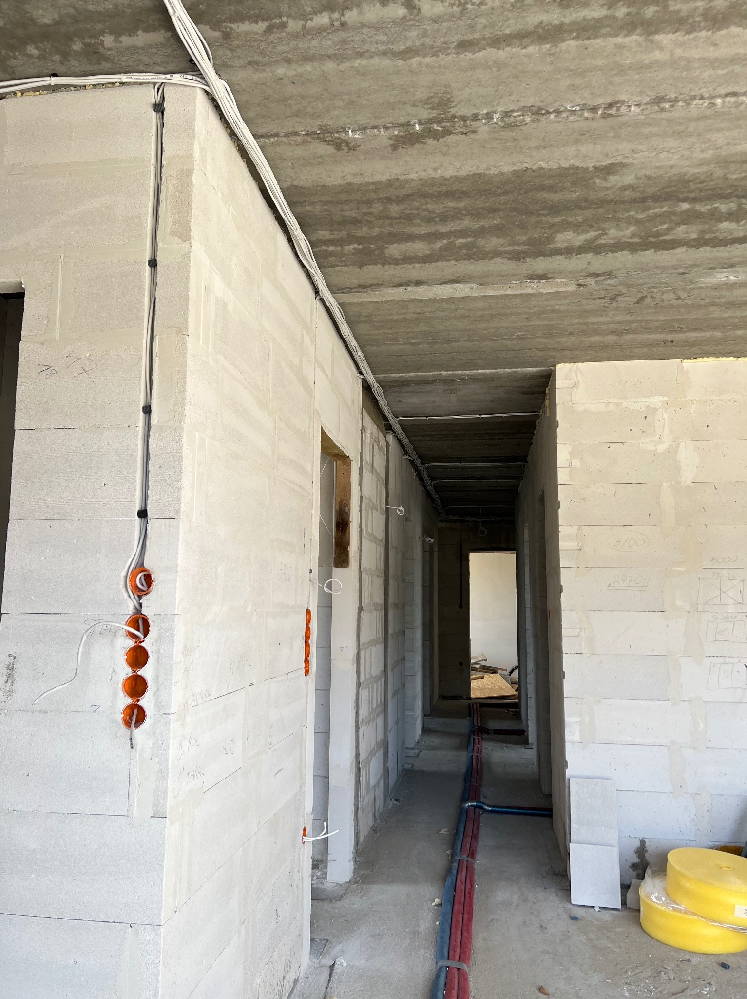 Wnętrze w stanie surowym: widoczne przewody elektryczne prowadzone po ścianach i pod sufitem, puszki instalacyjne w ścianach, instalacja wodna na podłodze, ściany z betonu komórkowego z odręcznymi...