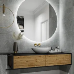Nowoczesna łazienka z okrągłym lustrem podświetlanym LED, umywalką nablatową i szafką z drewnianymi frontami na tle szarych płytek imitujących beton.