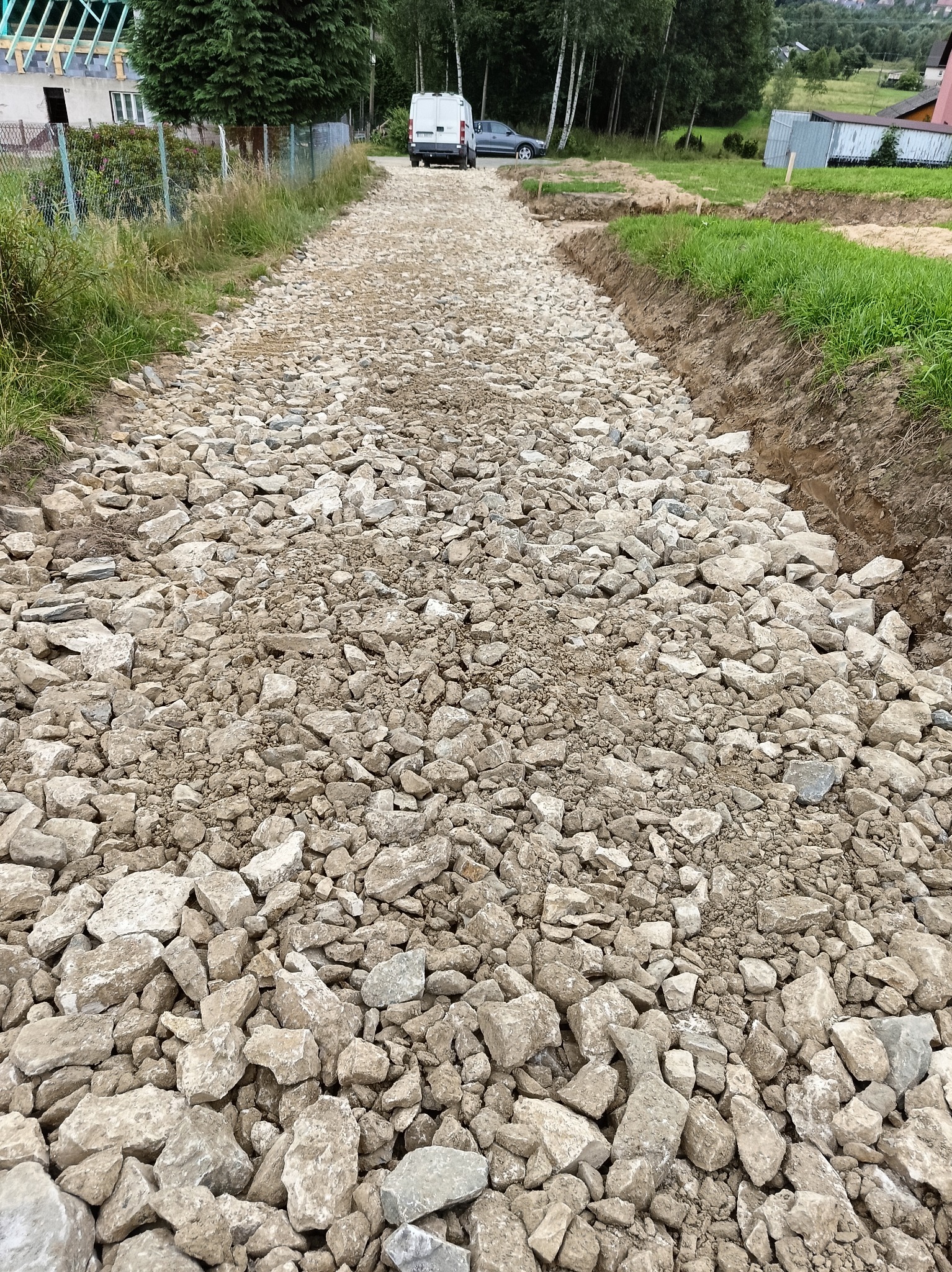 Droga gruntowa wysypana kruszywem, przygotowana pod budowę, z widocznym samochodem dostawczym w oddali.