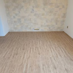 Doradztwo i obsługa techniczna Radosław Wojtczak - Wnętrze pokoju po remoncie: ułożone panele podłogowe w odcieniach jasnego drewna i ściana wykończona dekoracyjną płytką imitującą kamień w beżowo-szarej kolorystyce, widoczne gniazdka elektryczne.