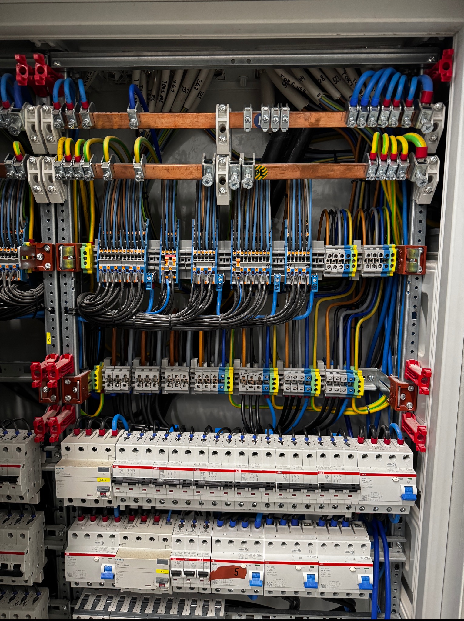 Rozdzielnia elektryczna z precyzyjnie ułożonymi przewodami, listwami zaciskowymi i zabezpieczeniami. Widoczne kable w różnych kolorach i oznaczenia na aparatach modułowych.