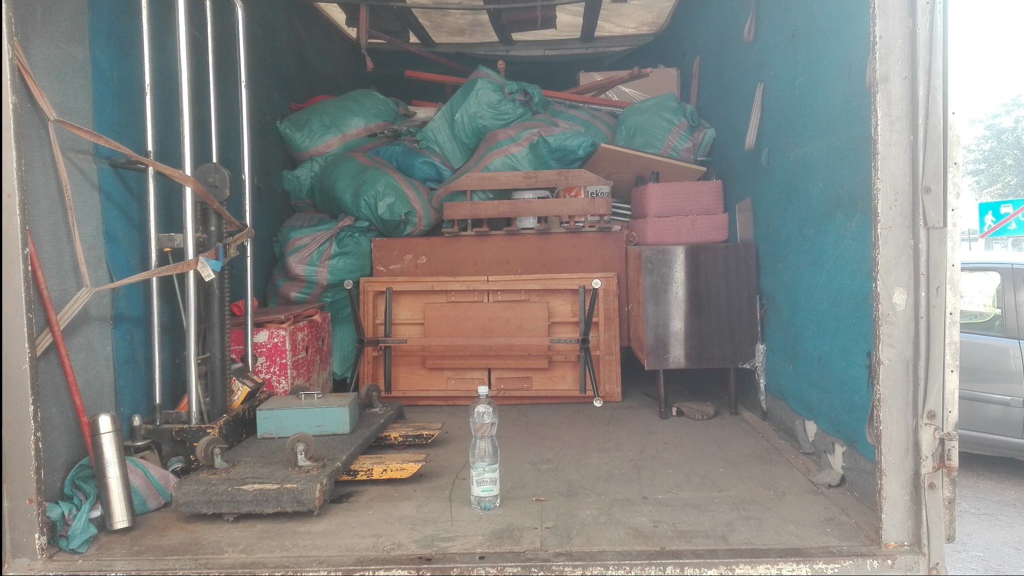 Wnętrze brudnej ciężarówki załadowane workami i meblami podczas transportu, butelka wody na podłodze.