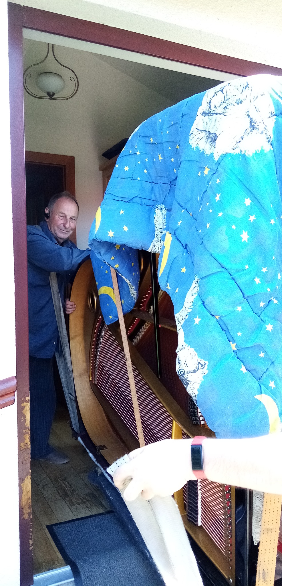 Mężczyzna uśmiecha się, trzymając zabezpieczony kocem fortepian podczas przeprowadzki.