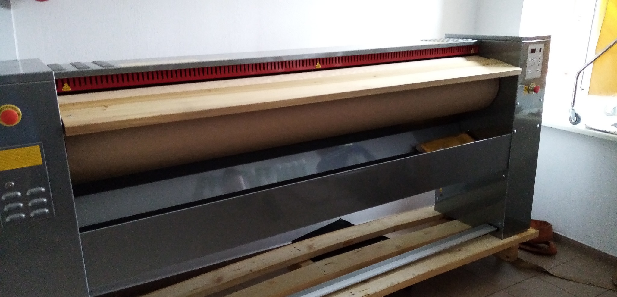 Duża, przemysłowa magielnica z rolką, panelem sterowania i ostrzeżeniami o zagrożeniu, ustawiona na drewnianej palecie.