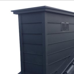 alpinmal - Metalowy komin wentylacyjny w kolorze antracytowym, zamontowany na dachu pokrytym ciemną dachówką, z widocznymi kratkami wentylacyjnymi.