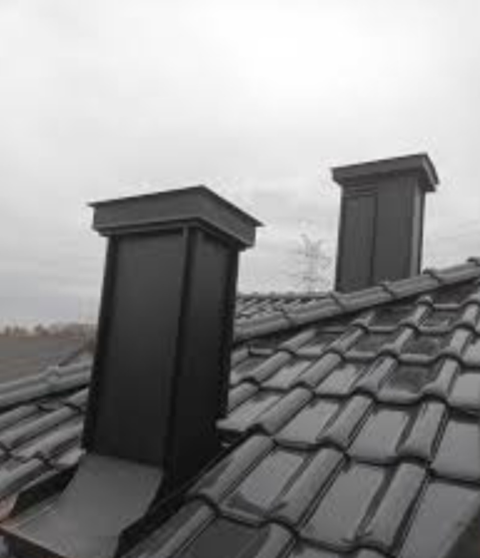Błyszczący, ciemny dach z dachówki ceramicznej z dwoma nowymi, czarnymi kominami na tle pochmurnego nieba.