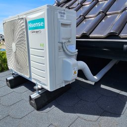 EMC Elektromechanika Chłodnicza - Zewnętrzna jednostka klimatyzacji Hisense zamontowana na dachu pokrytym gontem bitumicznym, widoczne czarne podkładki tłumiące drgania i elementy mocujące.
