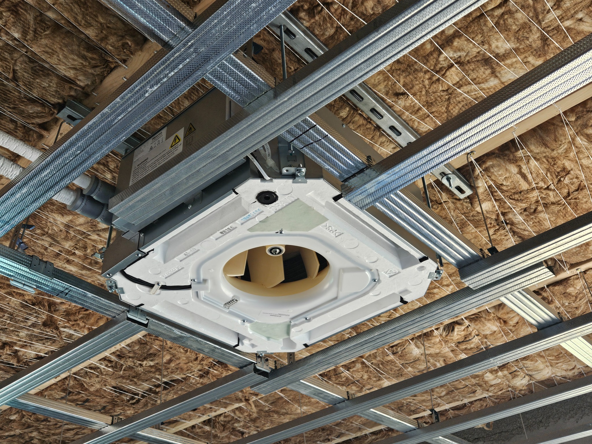 Kasetonowa jednostka klimatyzacyjna zamontowana w suficie podwieszanym z widoczną izolacją z wełny mineralnej, instalacja wentylacyjna w budynku biurowym lub komercyjnym.