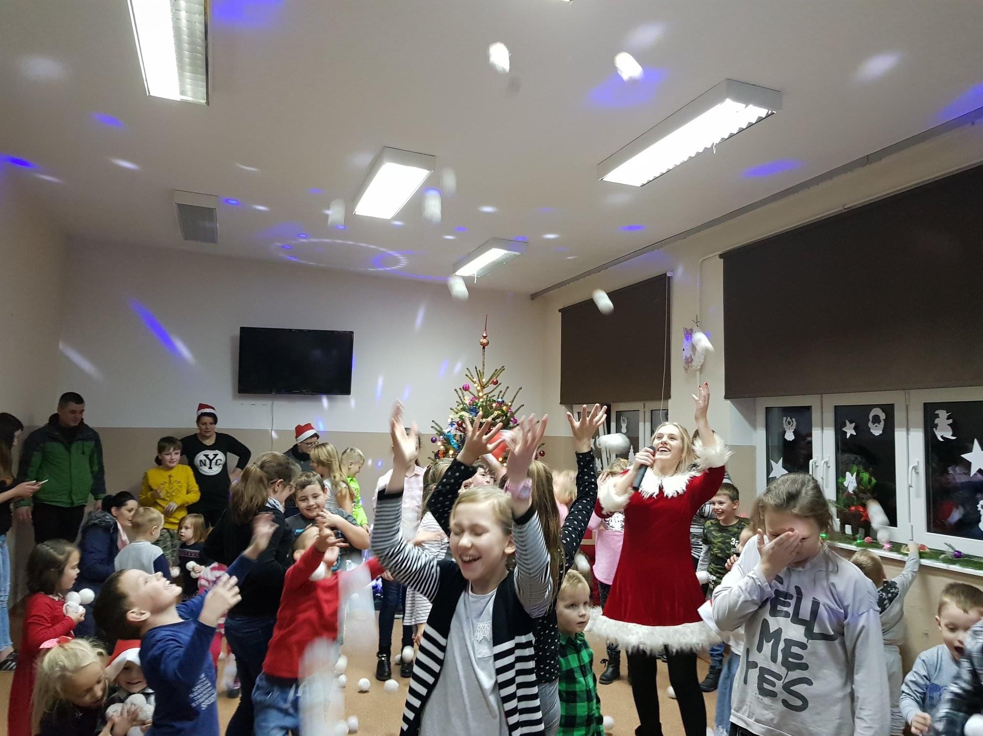 Świąteczna zabawa z animatorką w czerwonym stroju Mikołajki i grupą dzieci podczas eventu w Krakowie, w tle choinka i spadające sztuczne śnieżki.