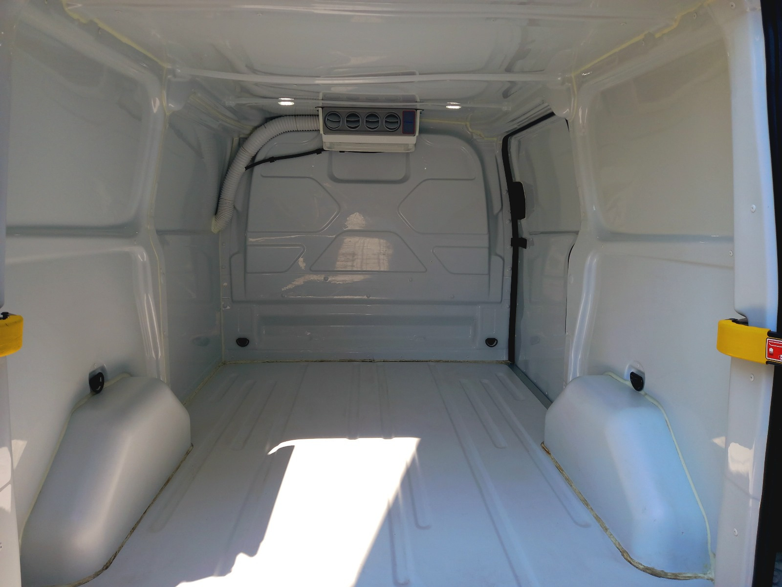 Wnętrze chłodni dostawczej: pusta przestrzeń ładunkowa z klimatyzacją, białe ściany i podłoga. Widok na tylne drzwi i system chłodzenia.