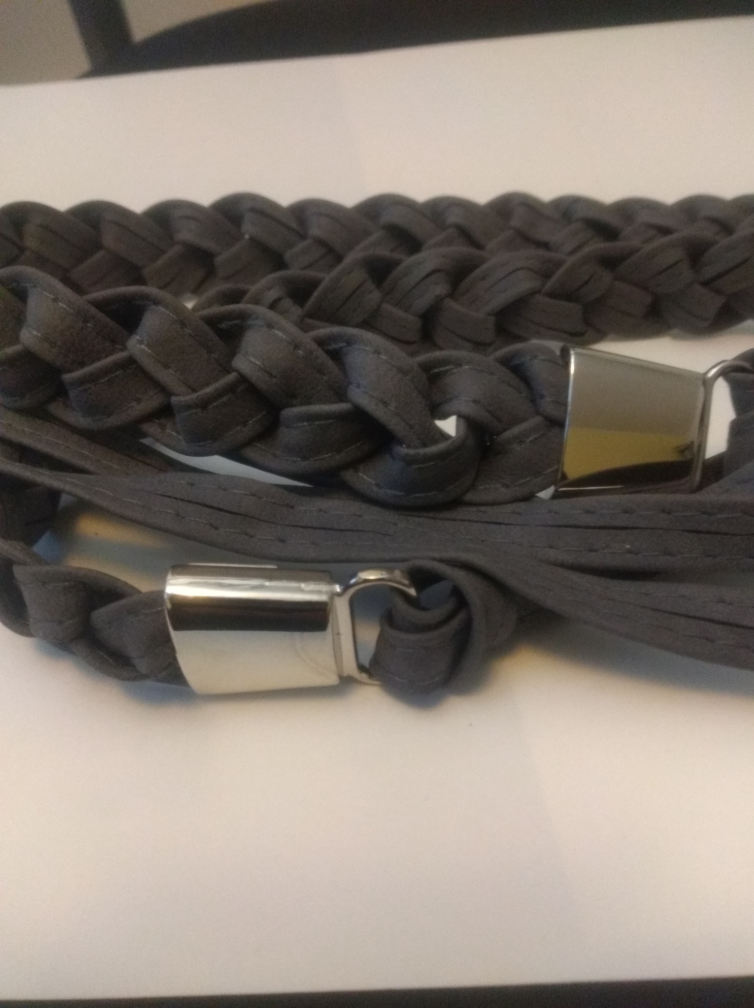 Szary, pleciony pasek damski z metalową sprzączką, leżący na białym tle.