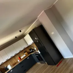 Nowoczesna kuchnia z białymi szafkami górnymi i grafitowymi dolnymi, drewnianym blatem i czarną lodówką; widoczny poziomica przy ścianie.