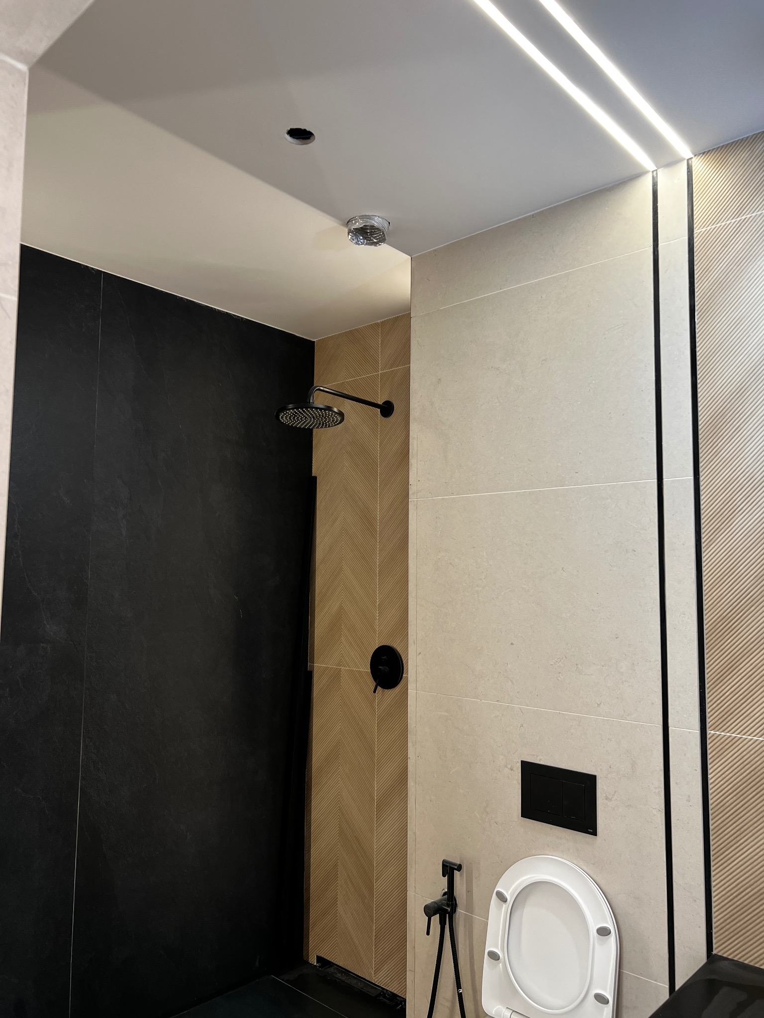 Nowoczesna łazienka z czarnymi i beżowymi płytkami, deszczownicą i podświetlanym sufitem LED, minimalistyczny design.