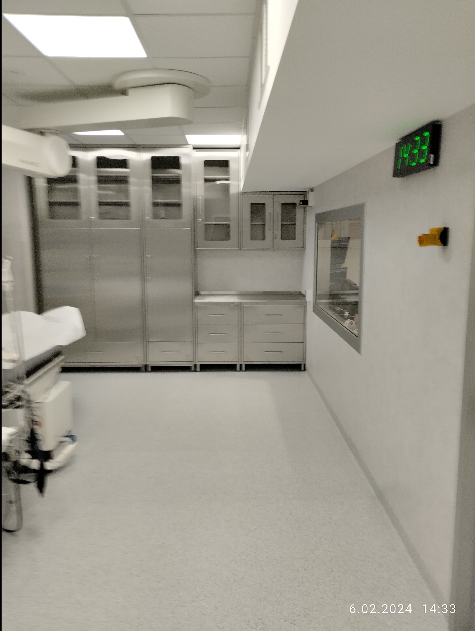 Wnętrze sterylnego pomieszczenia z metalowymi szafkami, cyfrowym zegarem na ścianie i sprzętem medycznym.