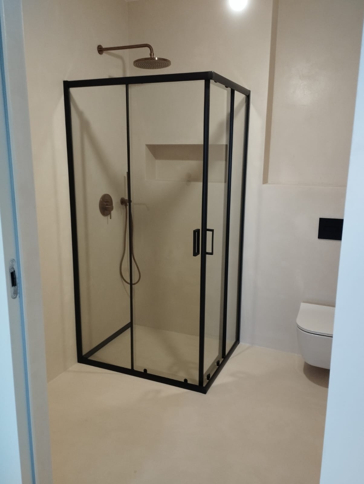 Nowoczesna kabina prysznicowa z czarnymi profilami, deszczownicą w kolorze miedzi i minimalistyczną armaturą w wykończonej łazience.