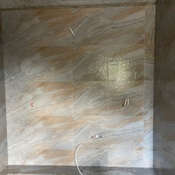 Remonty Serhii Bulava - Wykończona łazienka z płytkami imitującymi kamień, widoczne wyprowadzenia instalacji wodnej i elektrycznej. Na podłodze narzędzia glazurnicze.