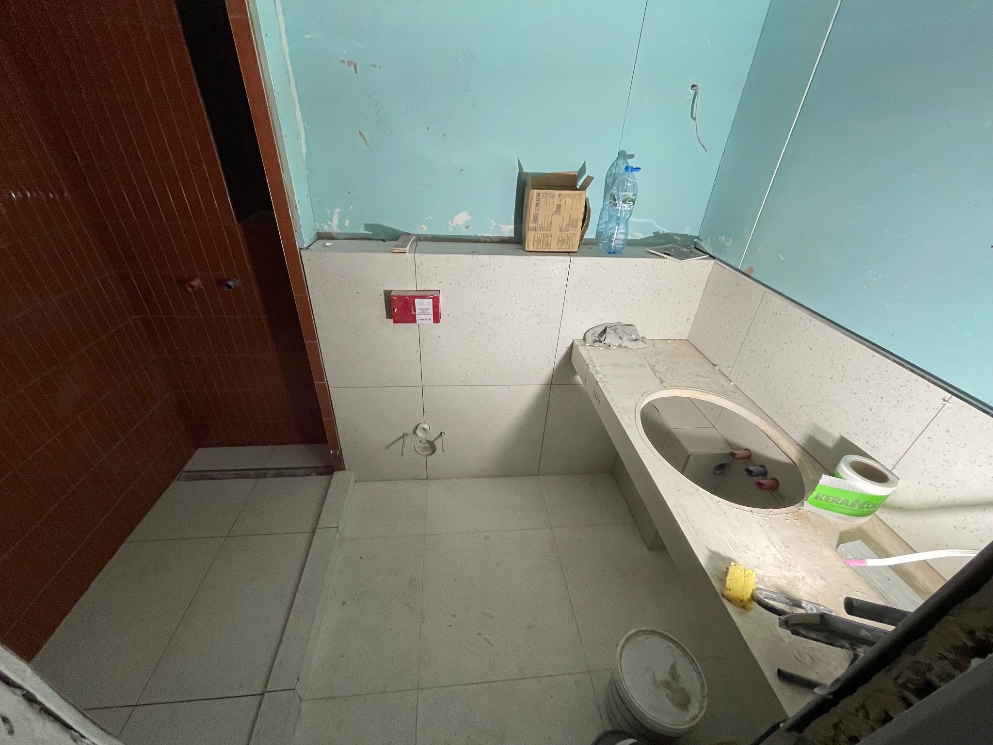 Łazienka w trakcie prac wykończeniowych: ułożona jasna glazura podłogowa i ścienna, widoczna zabudowa umywalki z wyciętym otworem, niebieska ściana z widocznymi śladami po remoncie, brązowe płytki...