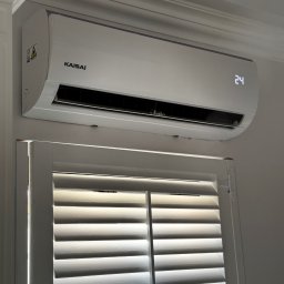 SOLFAN SPÓŁKA Z OGRANICZONĄ ODPOWIEDZIALNOŚCIĄ - Biały klimatyzator Kaisai zamontowany nad oknem z żaluzjami w Olsztynie, wyświetlający temperaturę 24 stopnie Celsjusza.