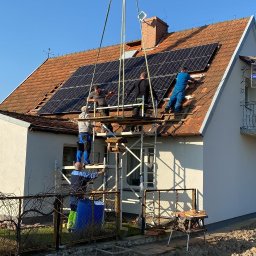 SOLFAN SPÓŁKA Z OGRANICZONĄ ODPOWIEDZIALNOŚCIĄ - Montaż paneli słonecznych na dachu domu jednorodzinnego z wykorzystaniem dźwigu i rusztowania, widoczne narzędzia pracy i ekipa montażowa w trakcie instalacji.