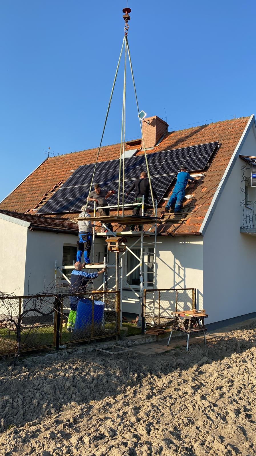 Montaż paneli słonecznych na dachu domu jednorodzinnego z wykorzystaniem dźwigu i rusztowania, widoczne narzędzia pracy i ekipa montażowa w trakcie instalacji.